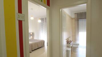 A hotel room with a bed, a bathroom with a toilet and sink, and a hallway with a sign indicating room number 3.