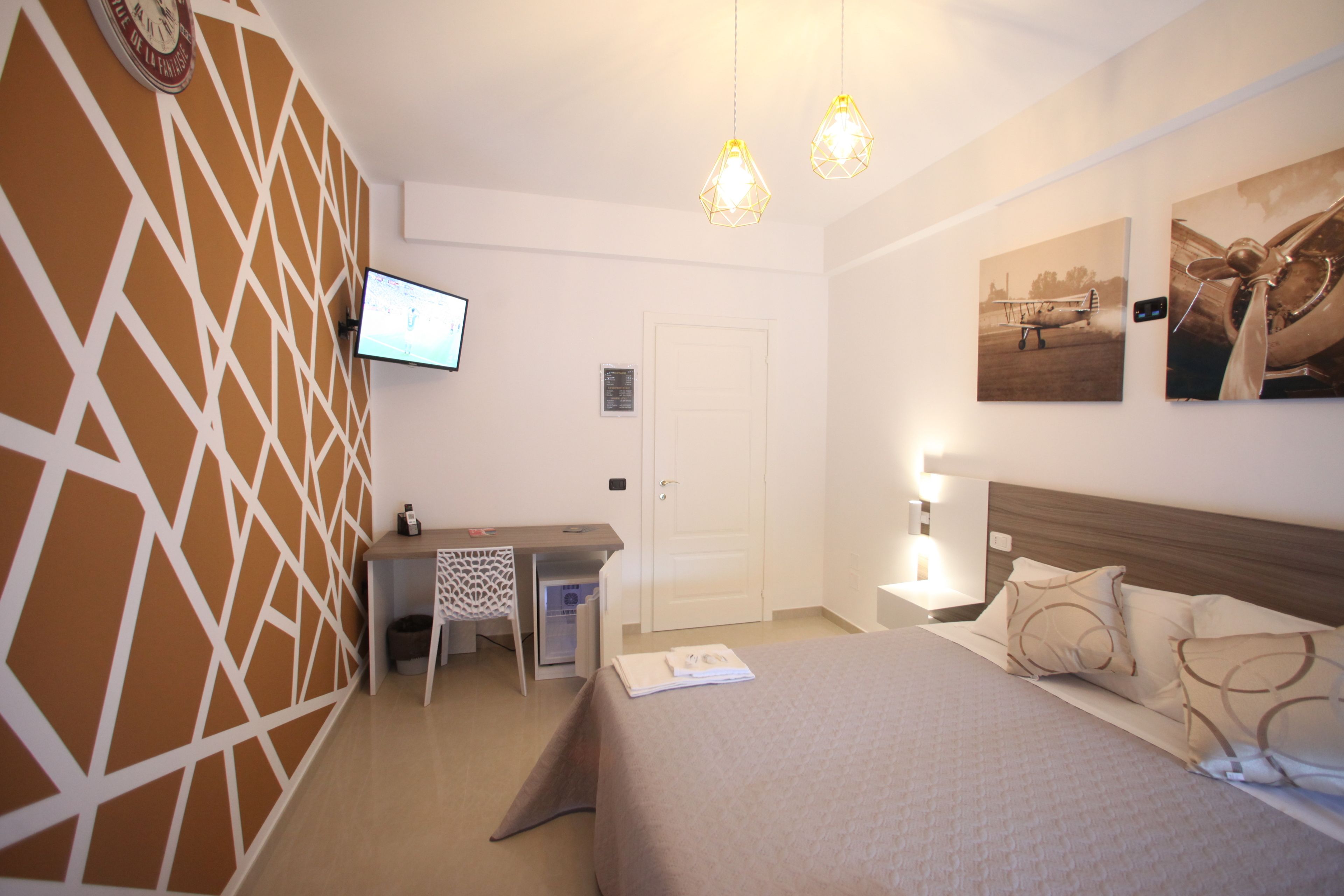 Une chambre d’hôtel équipée d’un lit, d’un bureau, d’une chaise, d’une télévision et d’œuvres d’art accrochées au mur.