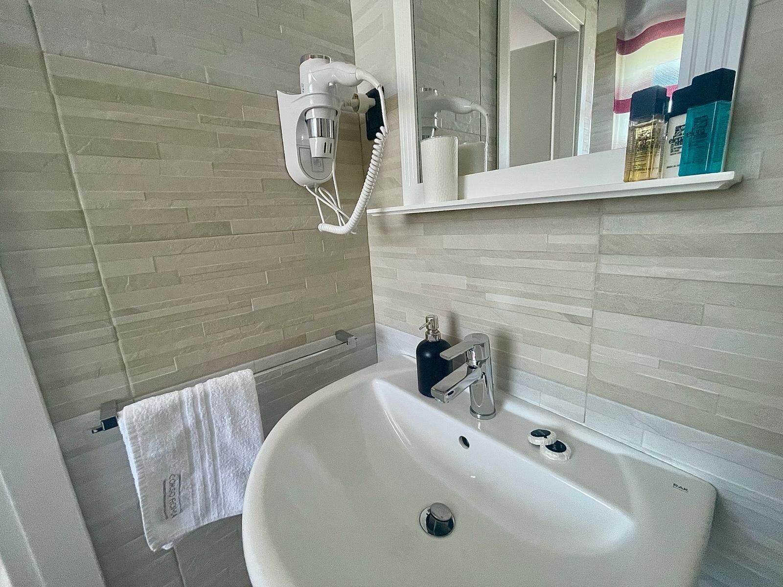 A bathroom with a white sink, a mirror, and a hairdryer mounted on the wall.