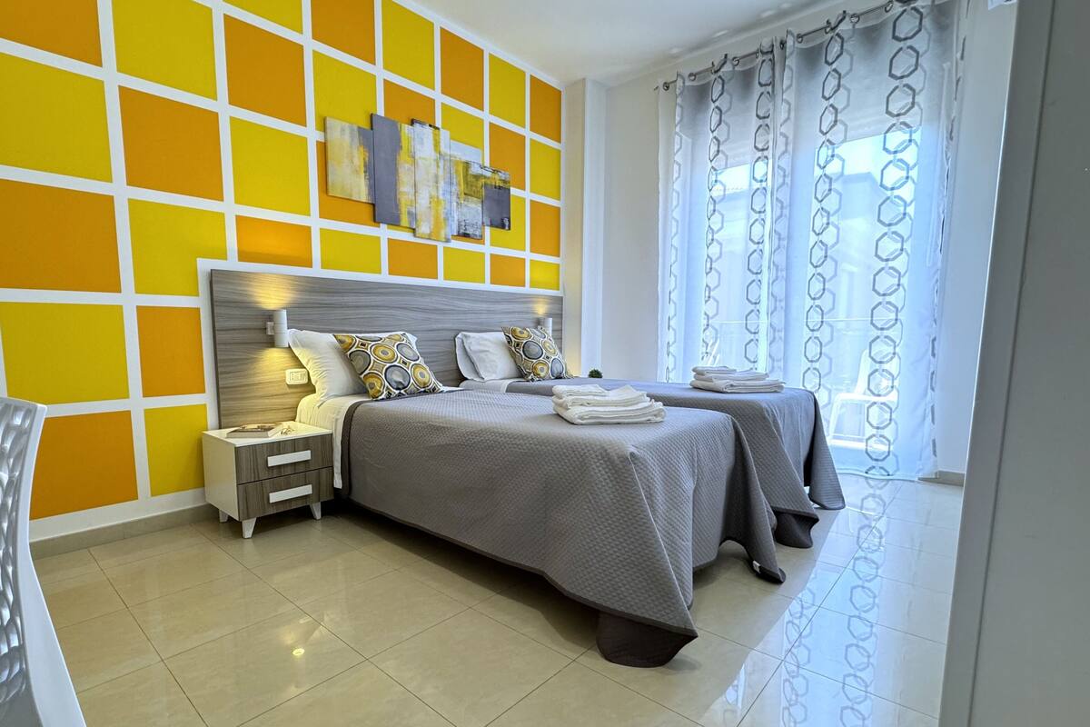 Une chambre d’hôtel moderne avec un grand lit, des tables de chevet, une chaise et une fenêtre avec des rideaux.