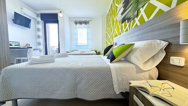 A hotel room with a bed, a desk with a laptop, a window with curtains, and a green decorative wall. - Bed & Breakfast Corso Roma (Apricena)
