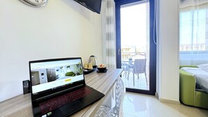 A laptop on a wooden desk, a flat-screen TV on the wall, a balcony with a view, and a bed with a green headboard. - Bed & Breakfast Corso Roma (Apricena)
