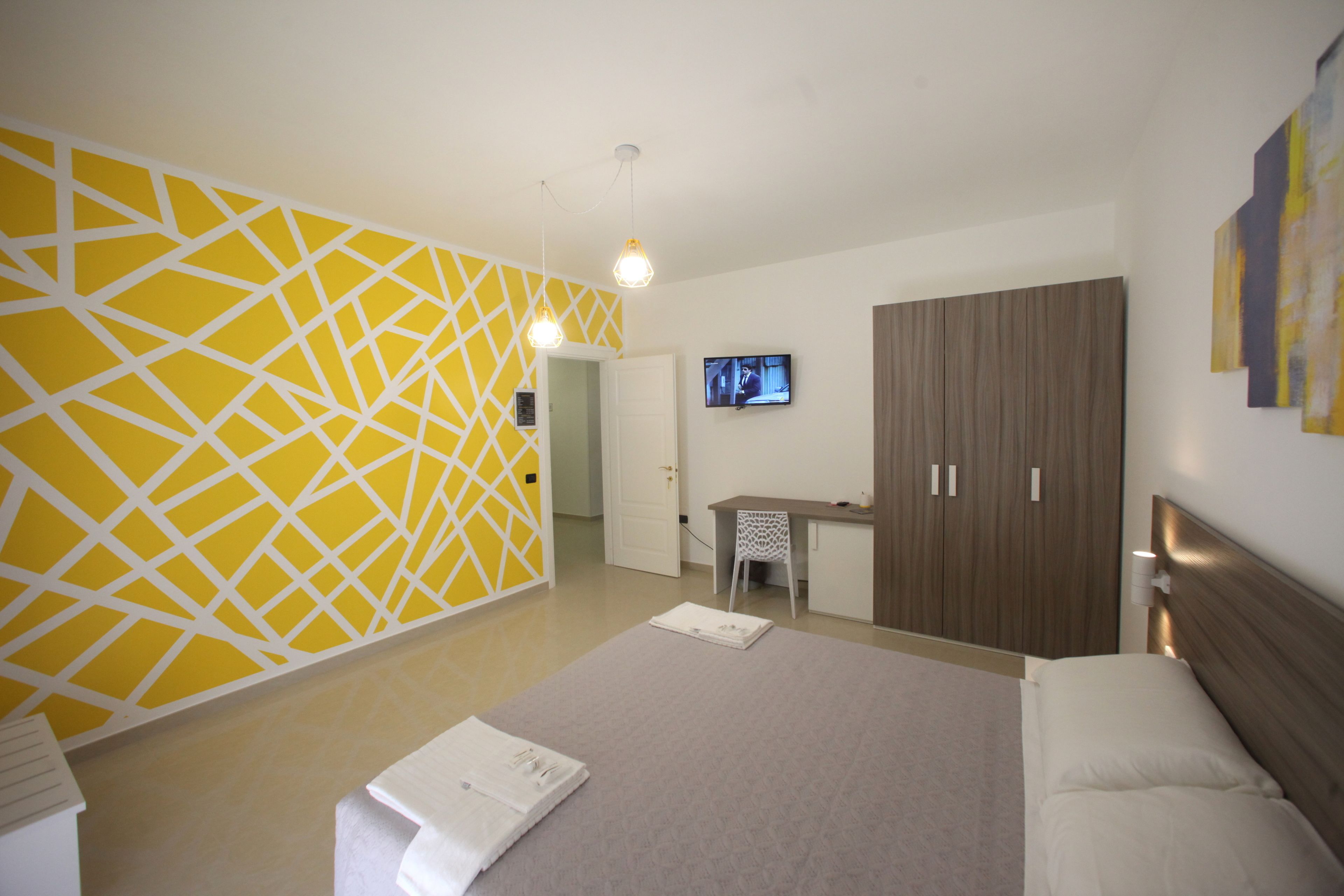 A hotel room with a bed, a desk, a chair, and a television on the wall.