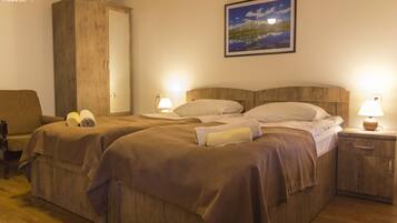 Un dormitorio con dos camas, cabeceros de madera, una mesita de noche con lámpara, un armario y un cuadro en la pared.