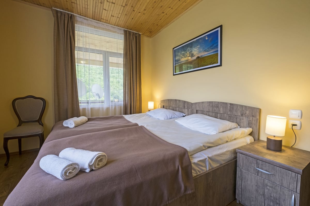 Ein Doppelbett mit zwei Kissen, ein Nachttisch mit Lampe, ein Sessel und ein Gemälde an der Wand.