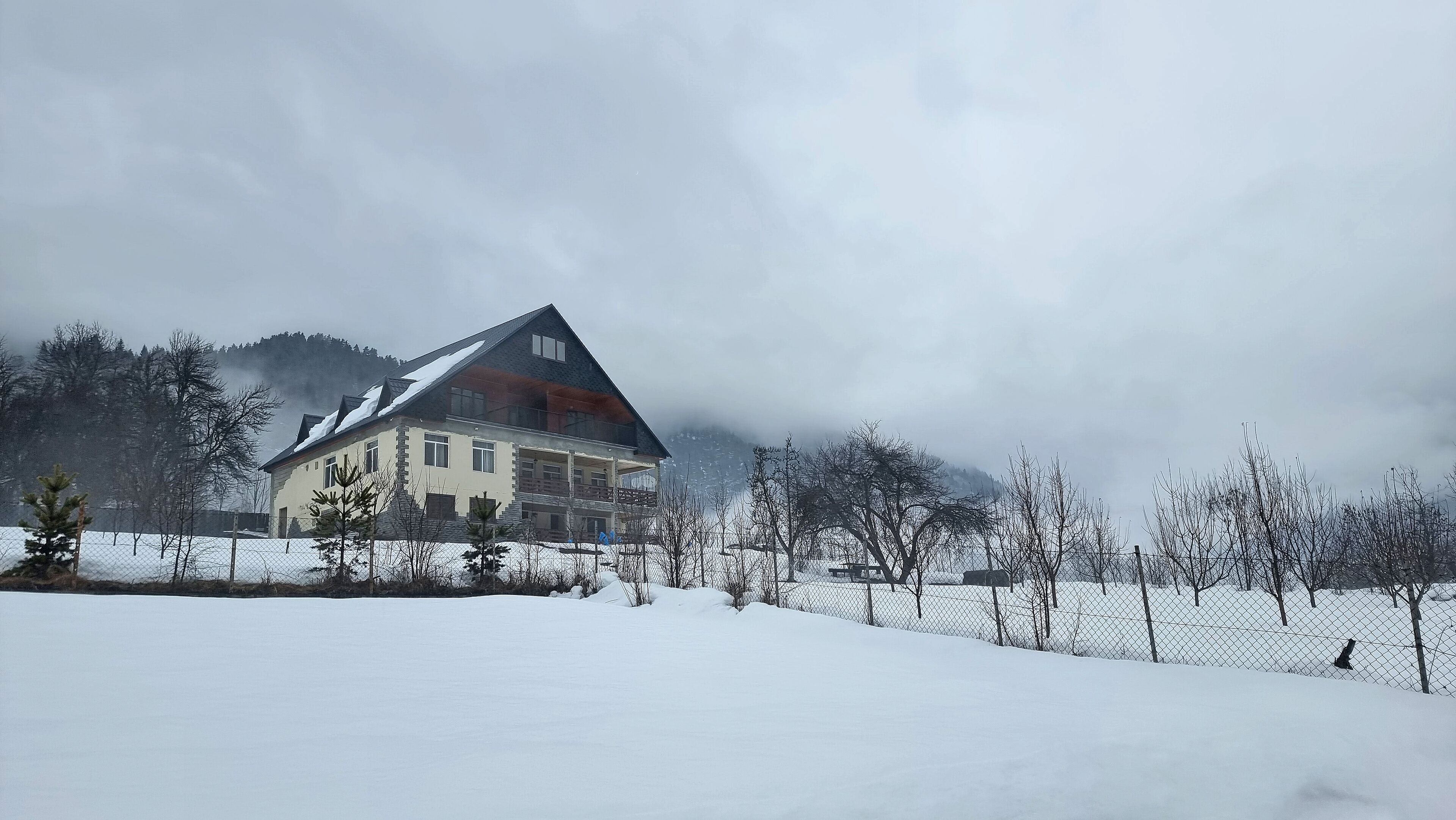 A house with a sloped roof, surrounded by snow-covered ground and trees.