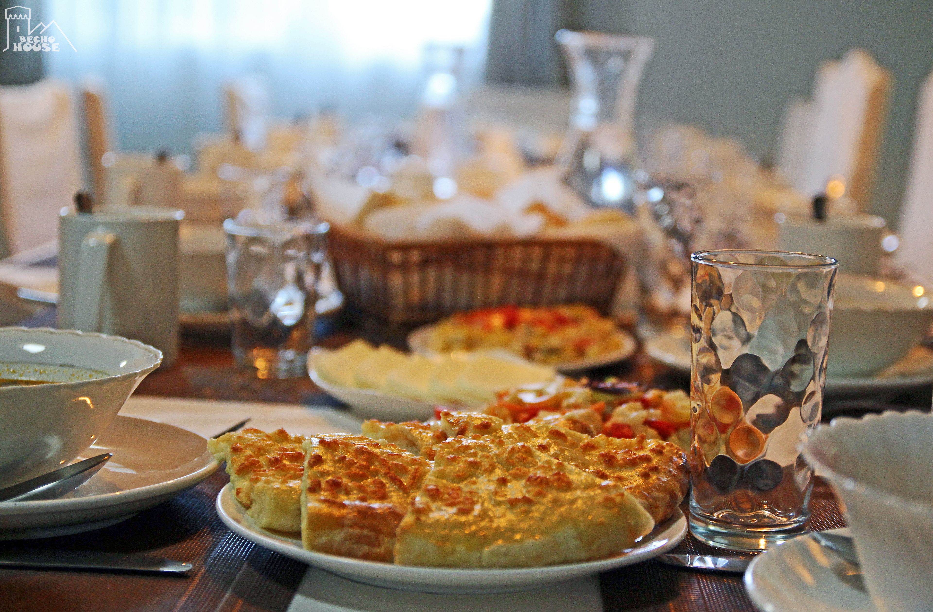 A dining table with plates of food, glasses, and a basket of bread.