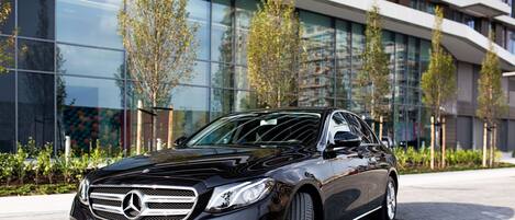 A black car parked in front of a modern building with glass windows and trees.