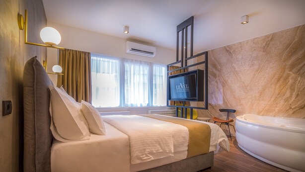 Una habitación de hotel moderna con una cama grande, televisor, bañera y vistas a la ciudad.
