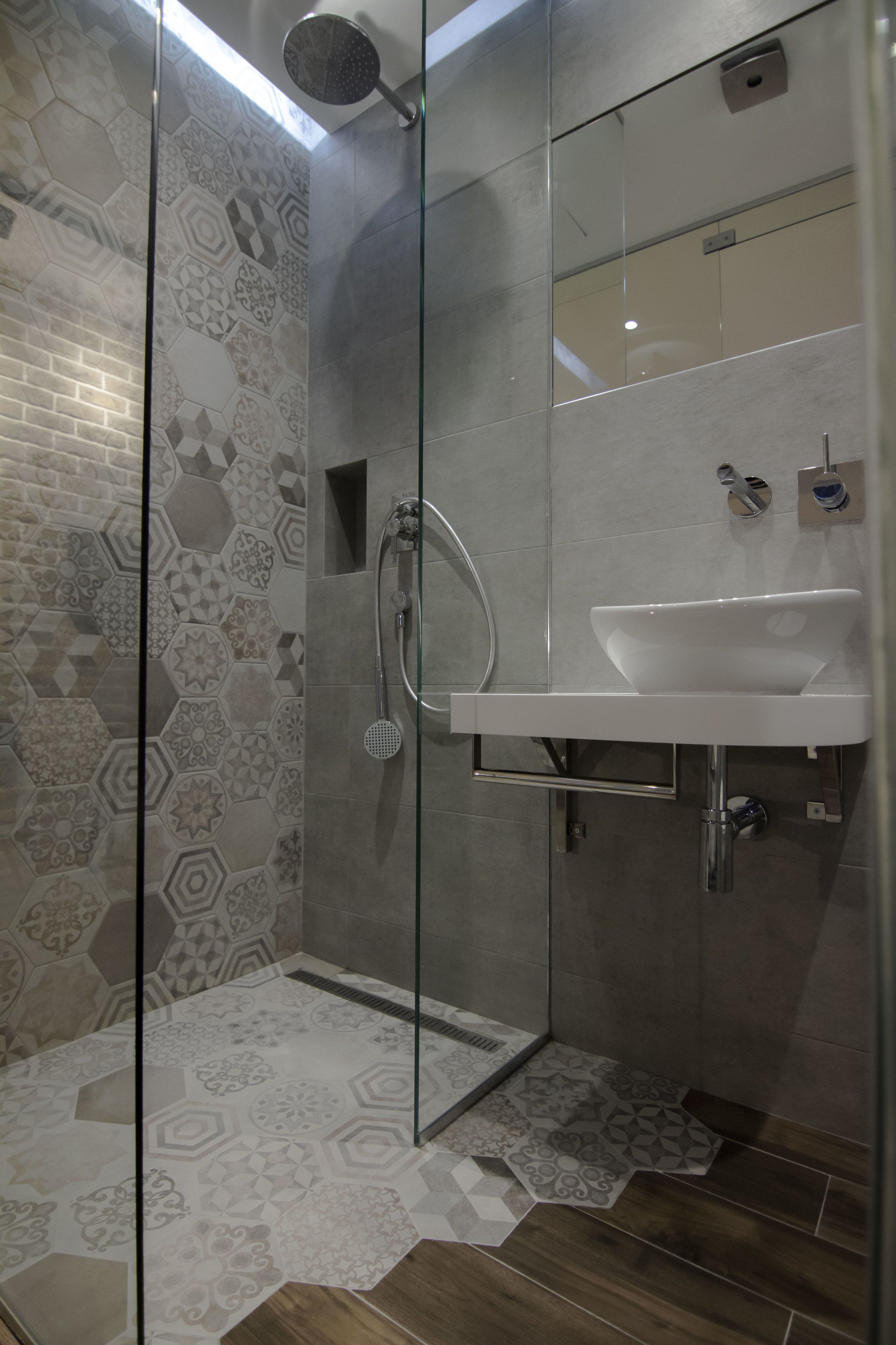 Un baño moderno con cabina de ducha de vidrio, lavamanos blanco y baldosas estampadas.