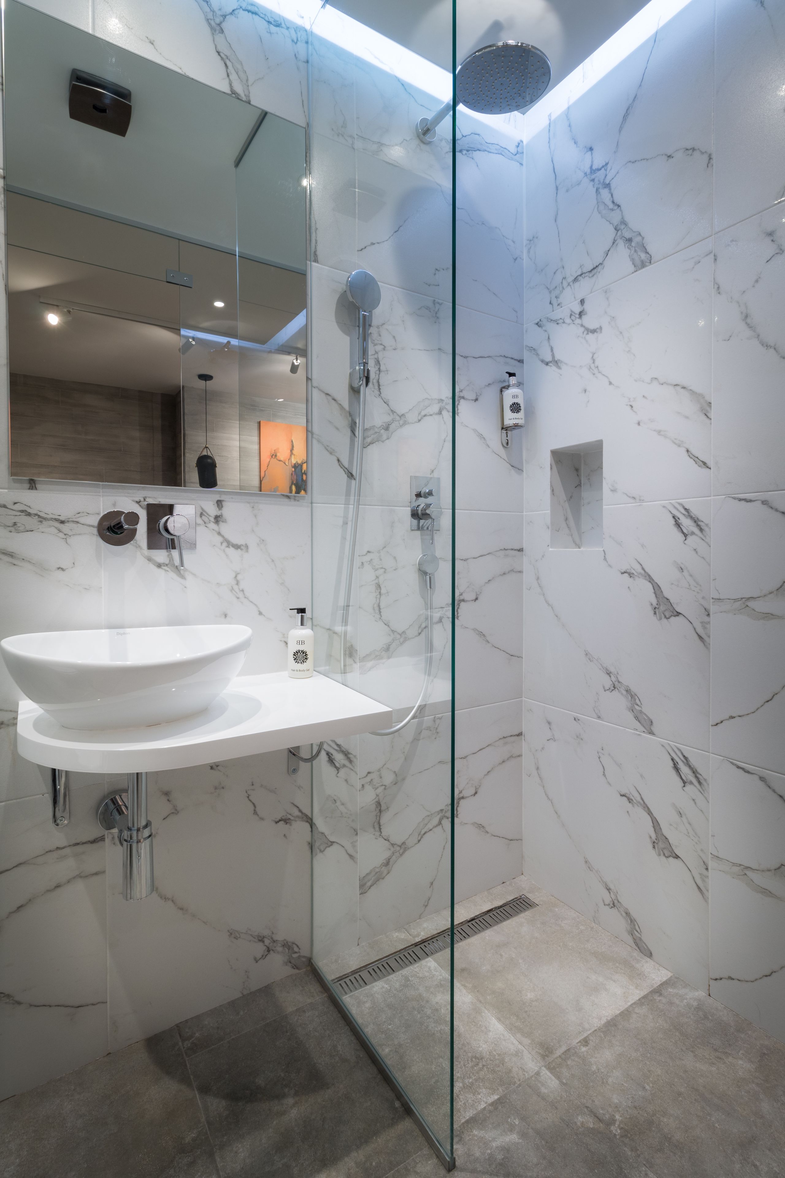 Un baño moderno con ducha de vidrio, lavamanos de mármol blanco y un espejo.
