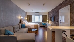 A modern hotel room with a sofa, a bed, a desk, and a television. - Level Luxury Suites (Belgrade)