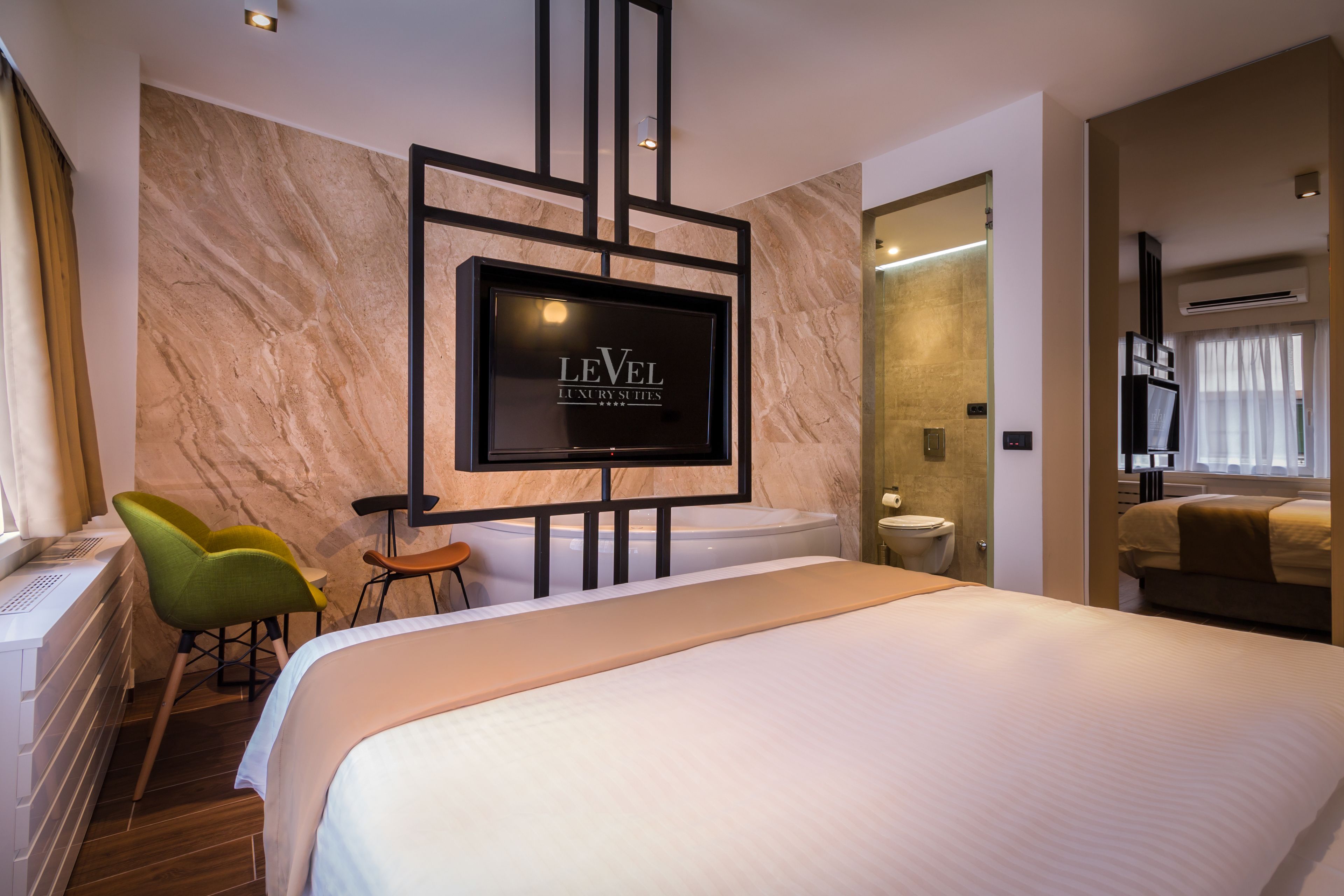 A modern hotel room with a large bed, a TV mounted on the wall, a desk with a chair, and a bathroom visible through an open door.