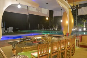Zona de bar con vistas a la piscina, taburetes y una mesa de billar.
