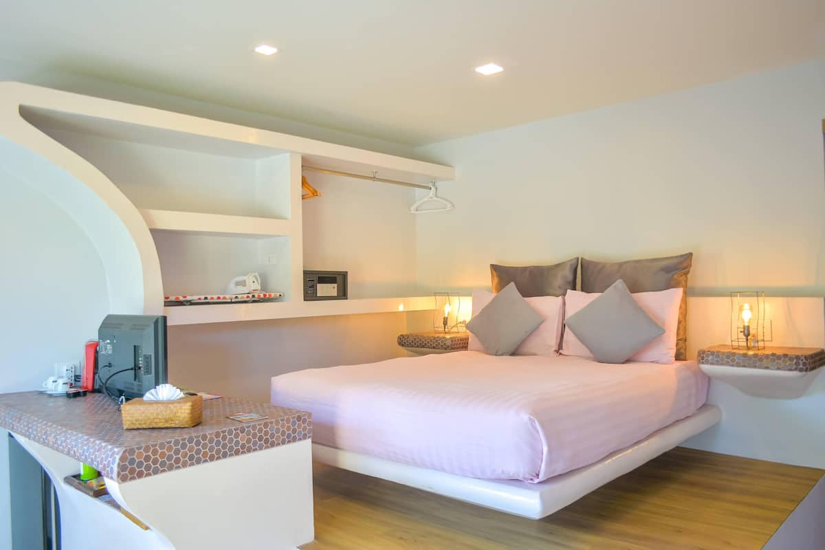 Un dormitorio moderno con cama, mesitas de noche, un escritorio con computadora y una percha para ropa.