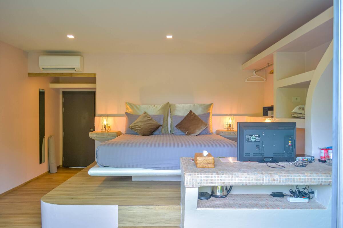 Un dormitorio moderno con cama, mesitas de noche, televisor y una pequeña zona de escritorio.