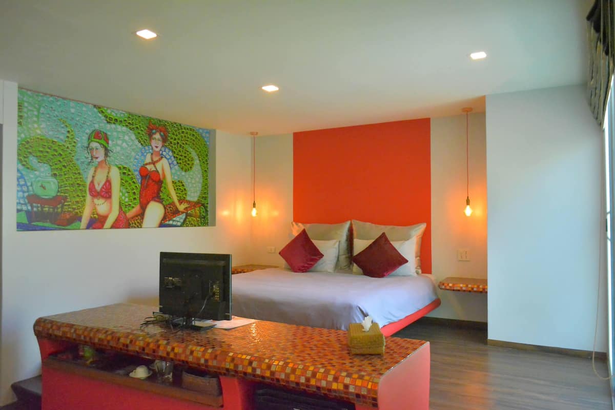 Una habitación de hotel con una cama, un escritorio, una computadora y un cuadro colorido en la pared.