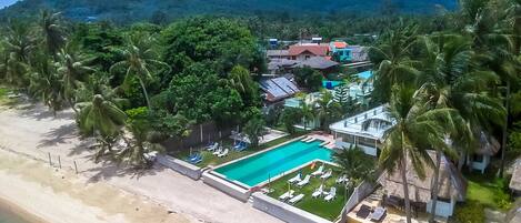 A resort with a swimming pool, palm trees, and a mountainous backdrop.