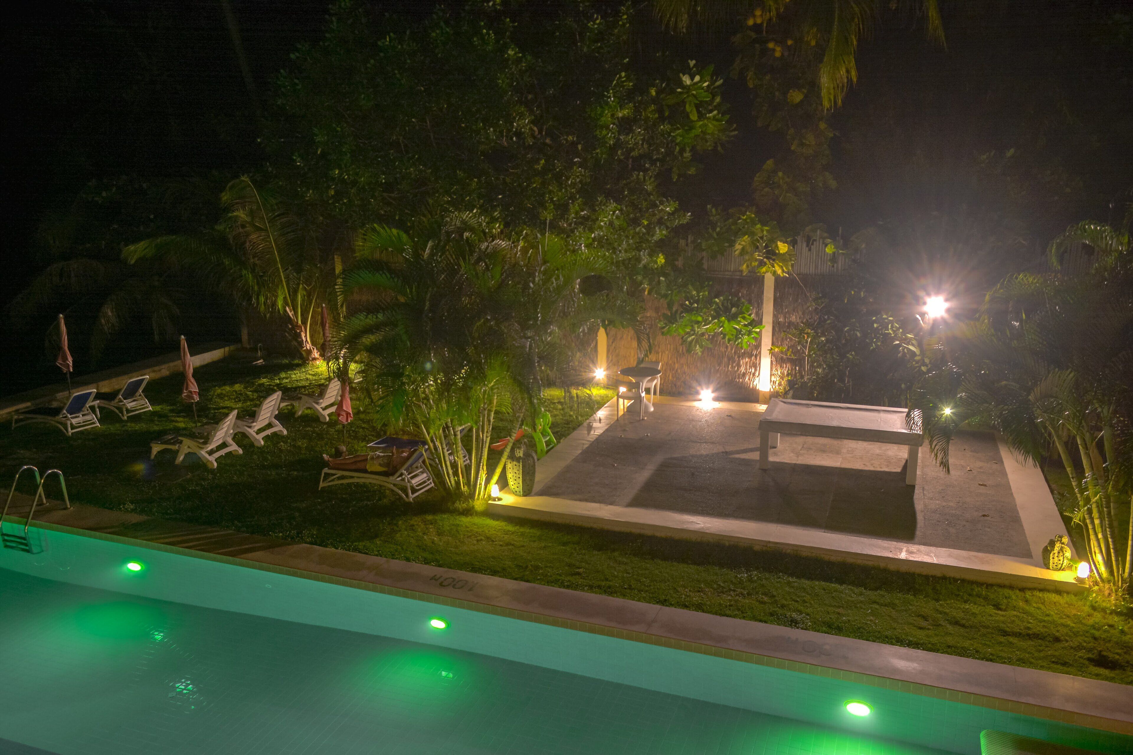 A nighttime view of a pool area with lounge chairs and a well-lit deck.