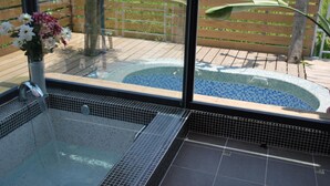 A glass-enclosed hot tub with a tiled floor, a wooden deck outside, and a potted plant with flowers. - Lotus Hostel Beicheng Zhuang (Luodong)
