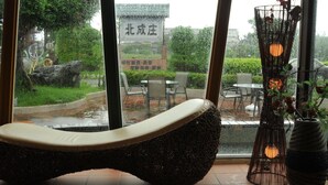 A modern lounge area with a unique woven chair, a large window with a view of a garden and a sign, and a decorative lamp. - Lotus Hostel Beicheng Zhuang (Luodong)