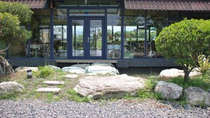 A modern building with large glass windows, a covered entrance, and a garden with rocks and plants. - Lotus Hostel Beicheng Zhuang (Luodong)