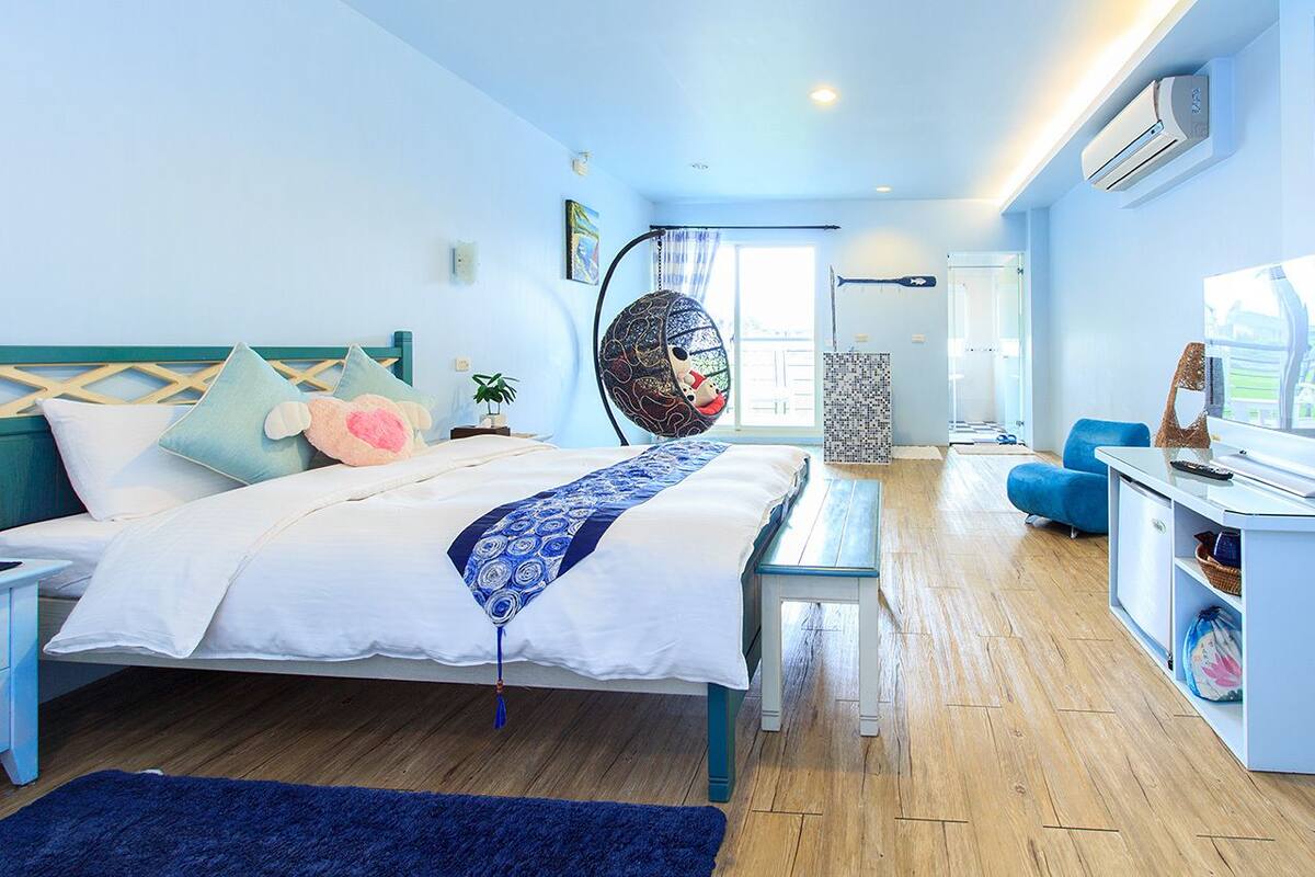 Quarto de hotel moderno com cama, cadeira suspensa, escrivaninha e televisão.