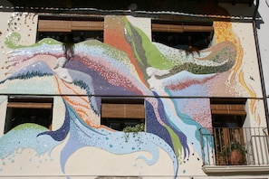 A building facade with a mosaic mural featuring abstract designs and a statue.
