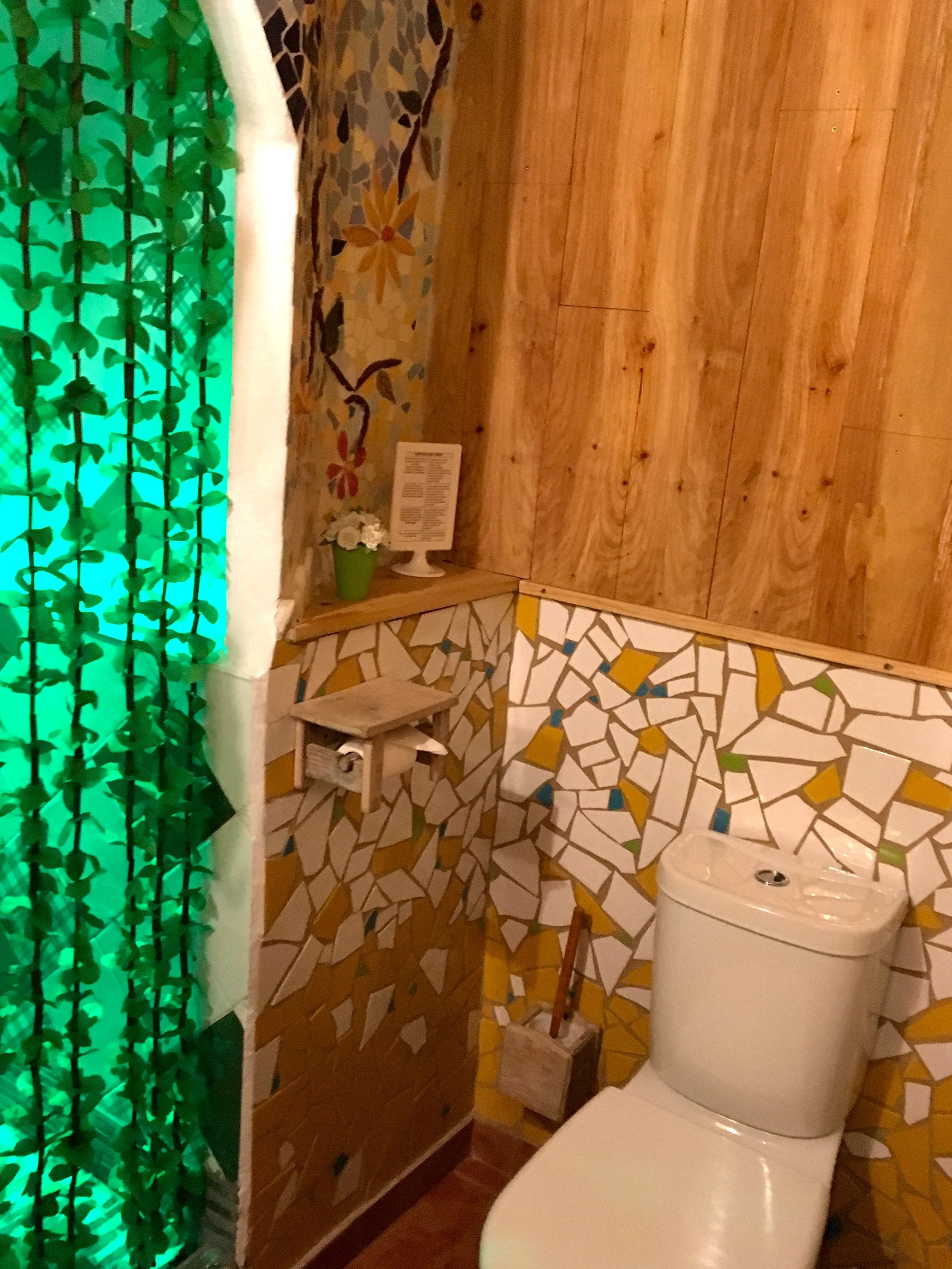 Un baño con pared de mosaicos, paneles de madera, un inodoro blanco y una planta verde.
