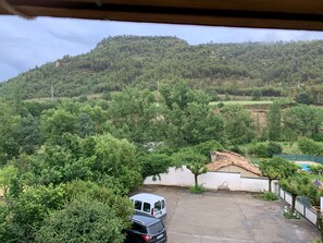 A parking area with a white van and a black SUV, surrounded by lush greenery and a hill in the background.
