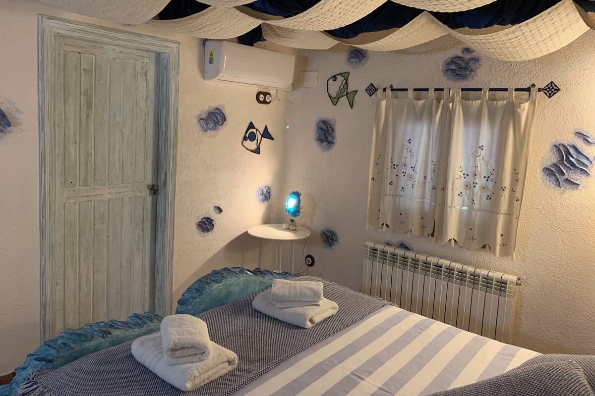 Quarto com cama, toalhas, ar condicionado fixado na parede, radiador e arte decorativa na parede.