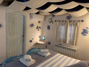 A bedroom with a bed, towels, a wall-mounted air conditioner, a radiator, and decorative wall art.
