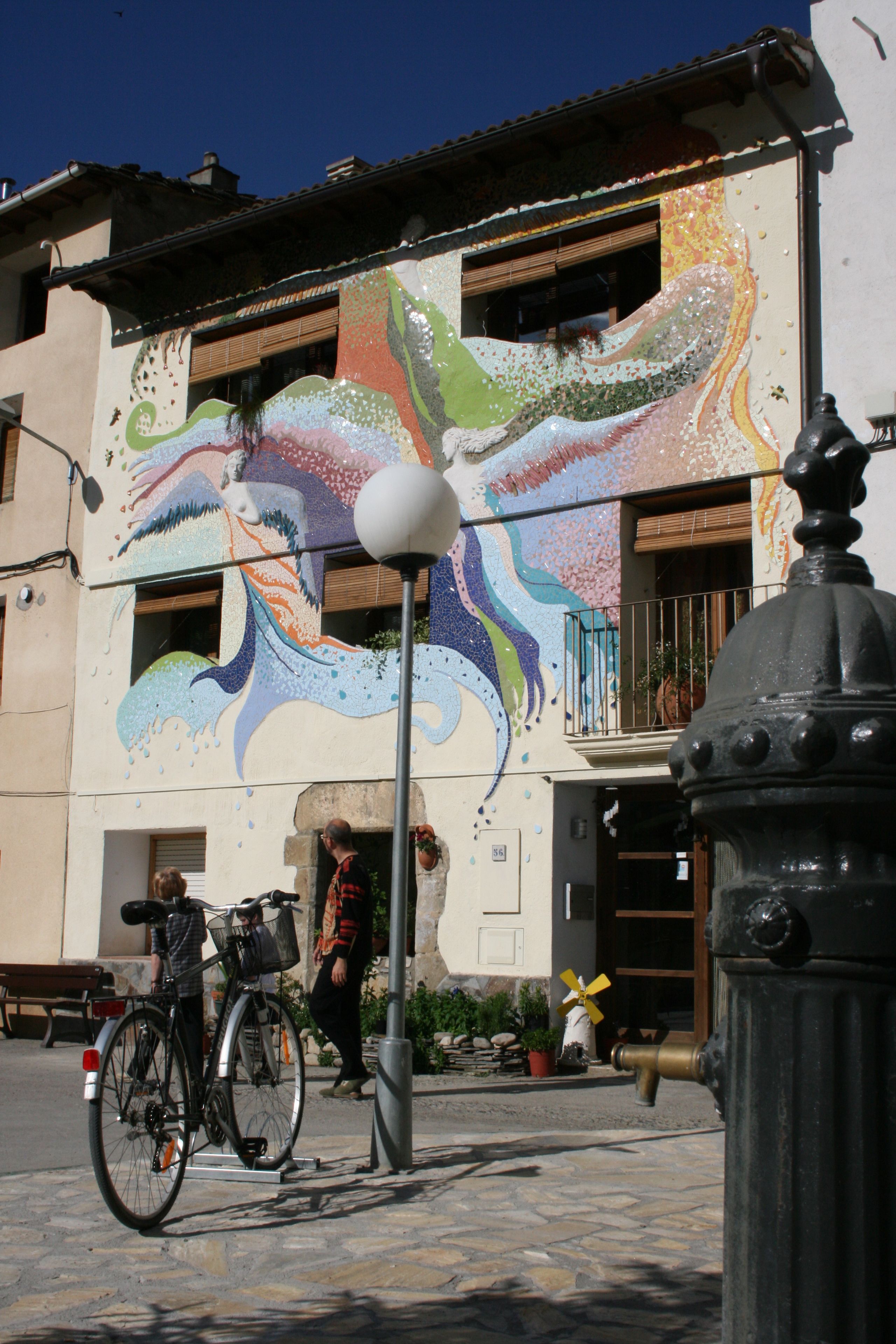 Un bâtiment orné d’une fresque colorée, un vélo garé devant et un lampadaire.