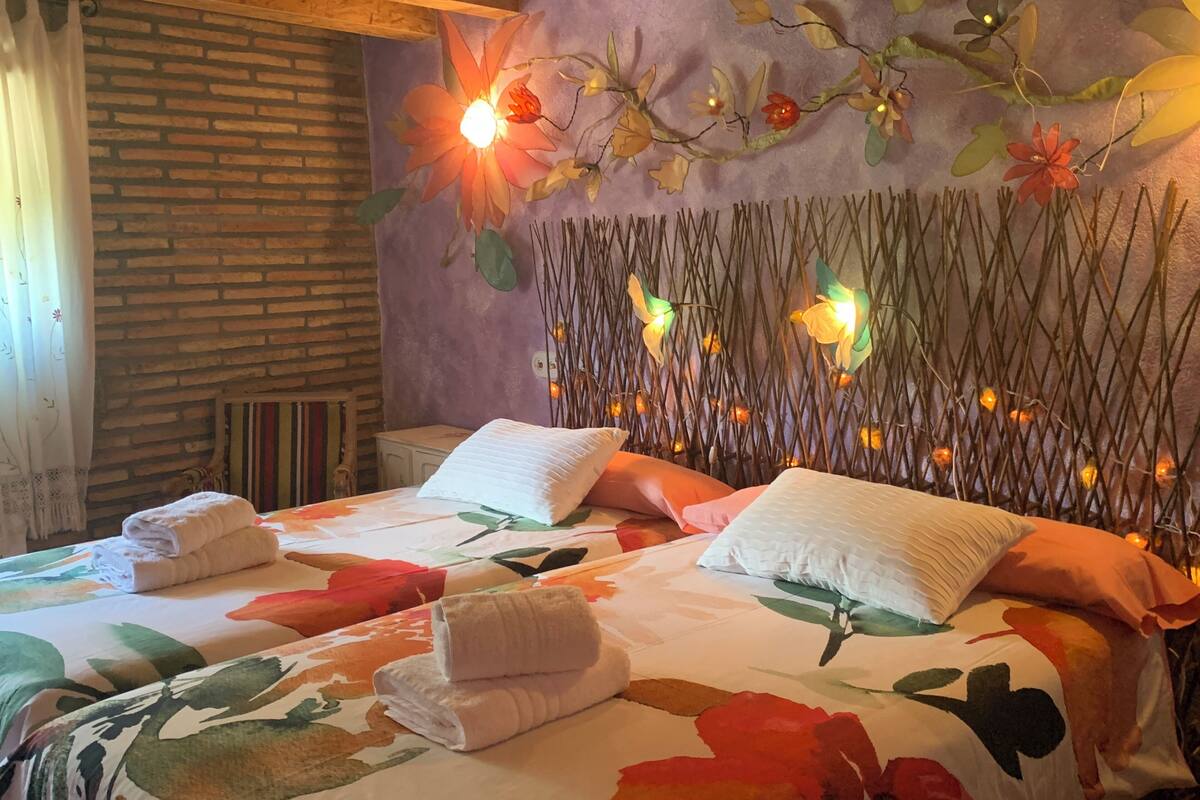 Quarto com parede de tijolos, cama com roupa de cama floral e parede decorativa com luzes.