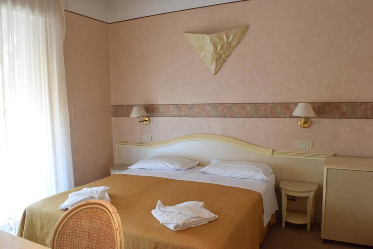 A hotel room with a bed, two bedside tables, a lamp, a decorative wall piece, and a chair.