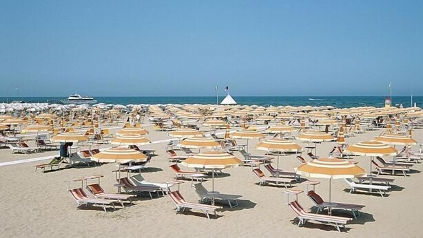 Une plage bordée de rangées de chaises longues et de parasols, un ciel dégagé et une vue lointaine sur la mer.