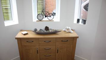 A wooden cabinet with drawers and a bowl on top, a window with a bicycle outside, and a small shelf with candles.
