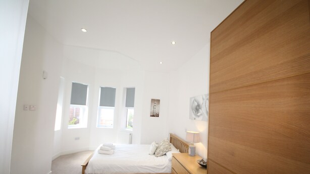 A bedroom with a bed, dresser, and a window with curtains. - Holiday Home With Hot Tub & Sauna (Bournemouth)
