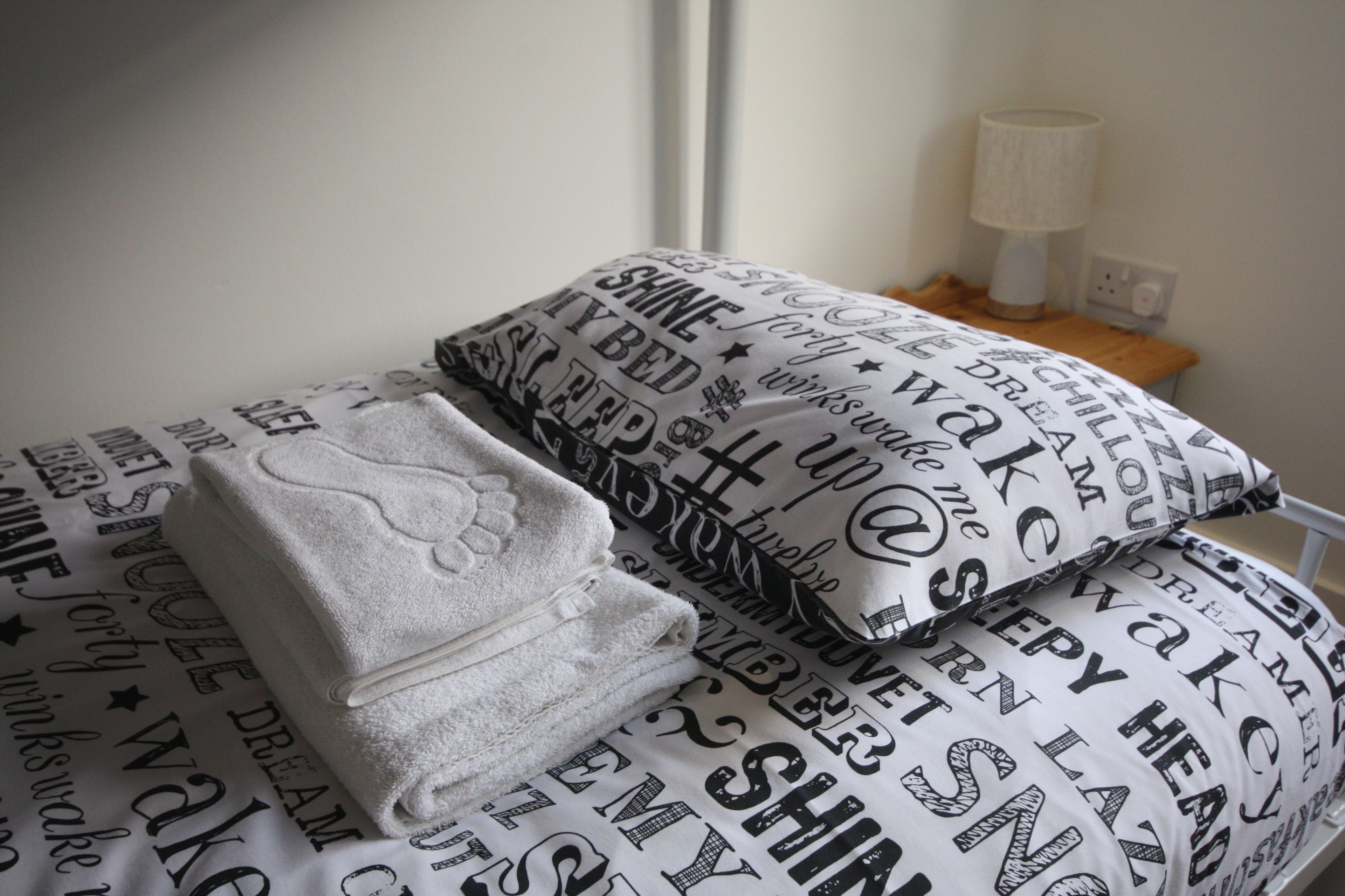 Cama bem arrumada com edredom branco e travesseiros com frases motivacionais.