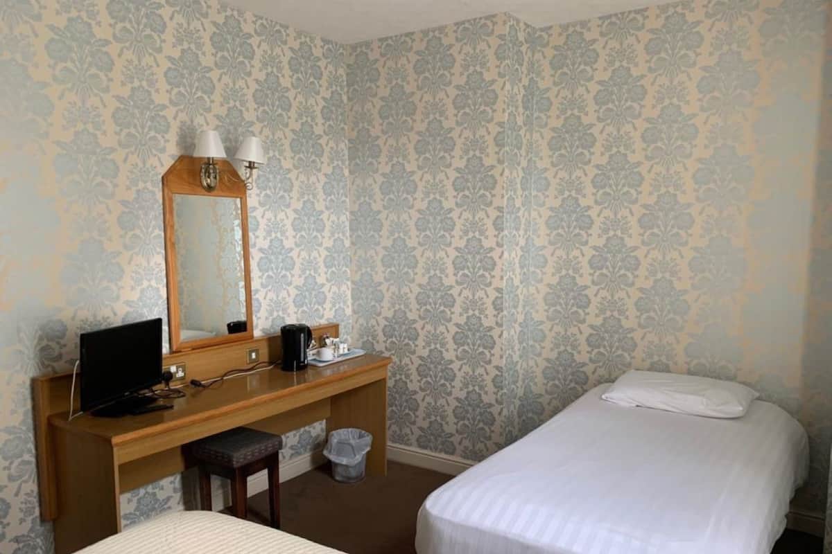 A hotel room with two beds, a wooden desk with a computer, a mirror, and a trash bin.