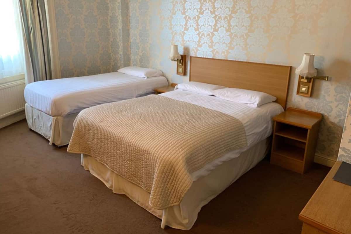 A hotel room with two single beds, a wooden nightstand, and a small table.