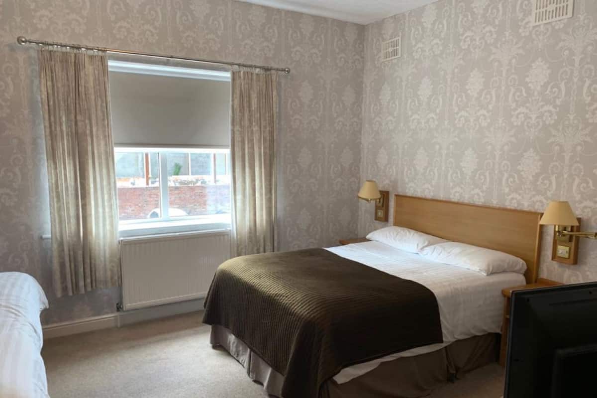 A hotel room with a bed, a window with curtains, a lamp, and a television.