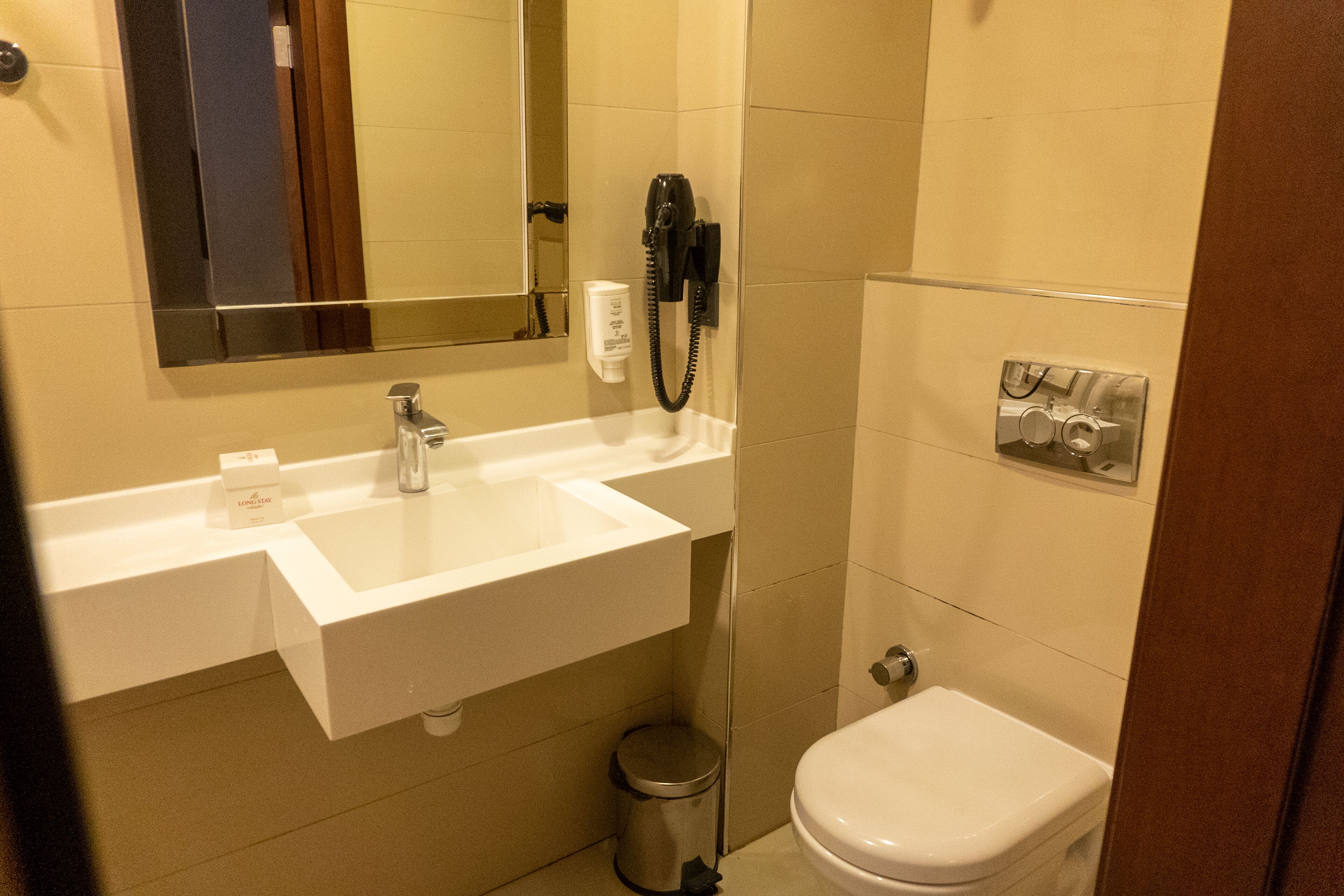 A bathroom with a white sink, a mirror, a hairdryer, a trash can, and a toilet.