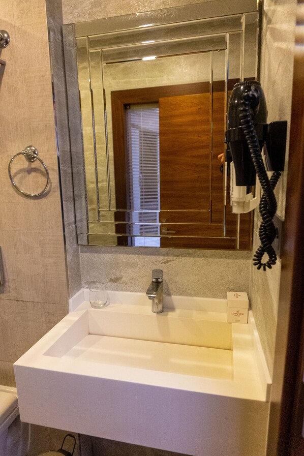 Un baño con un lavamanos blanco, un espejo y un secador de pelo montado en la pared.