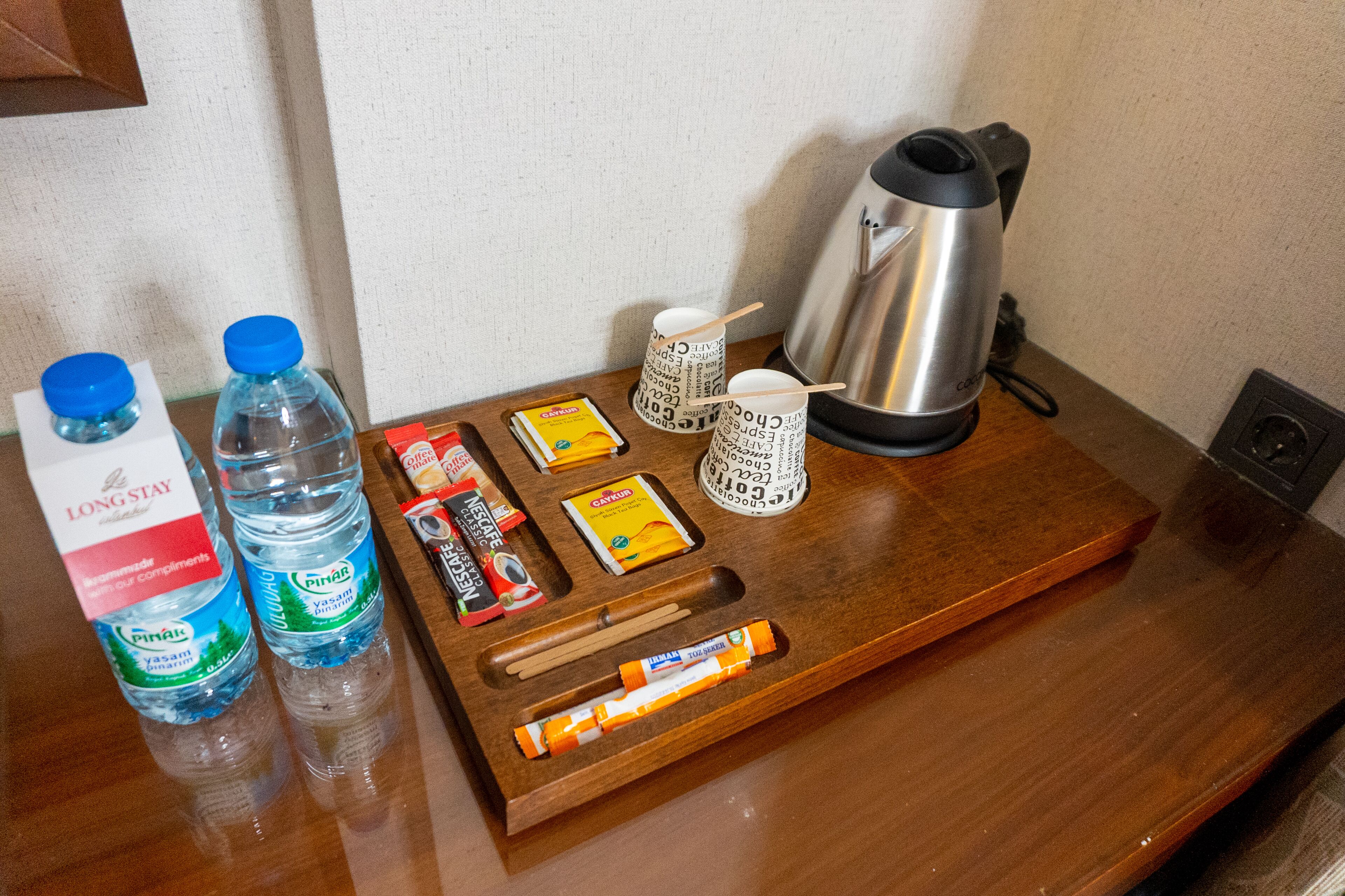 A wooden tray with a kettle, water bottles, a coffee maker, a grater, and some snacks.