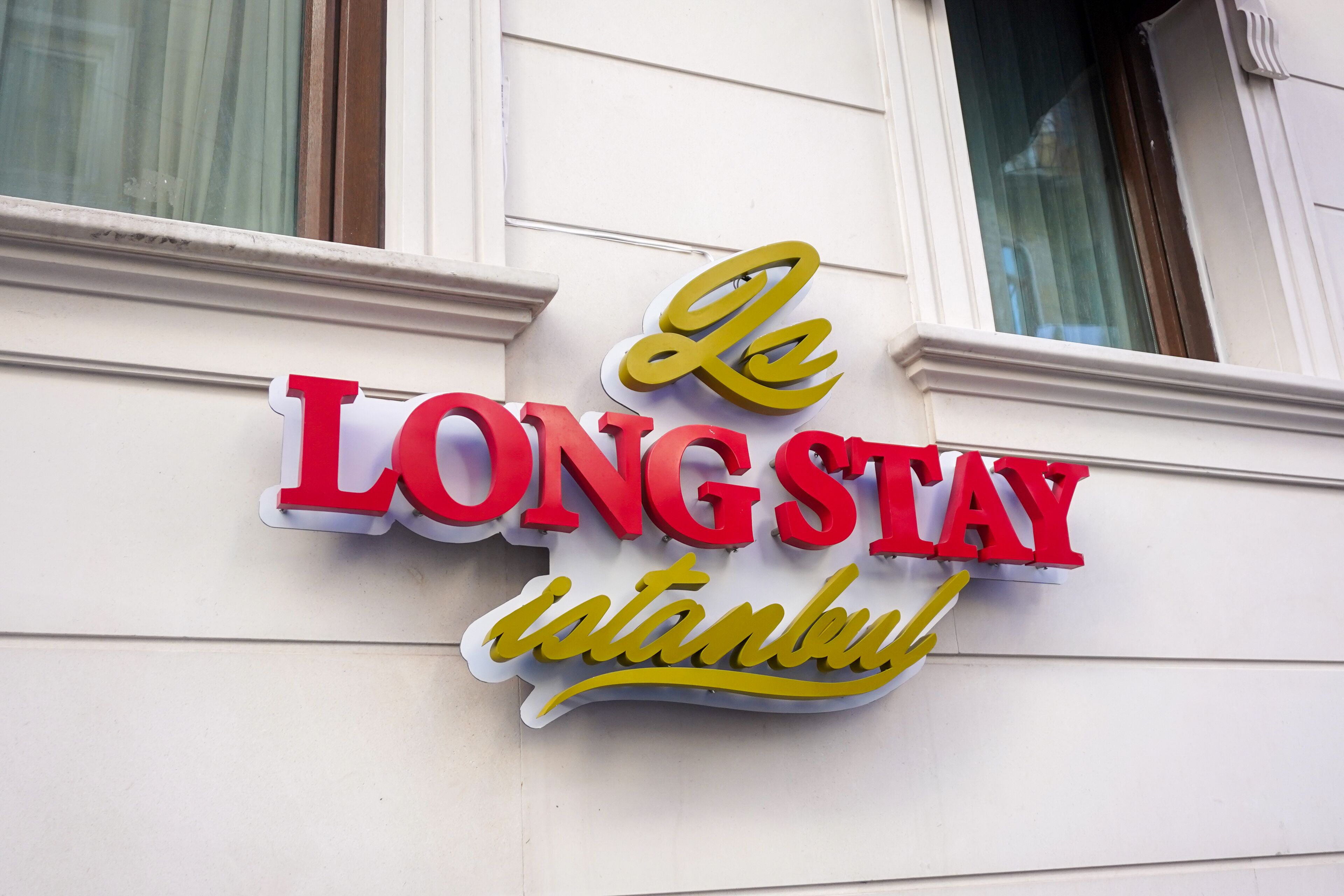 Une enseigne d’hôtel avec le nom « Le LONG STAY Istanbul » écrit en lettres rouges et jaunes en caractères gras.