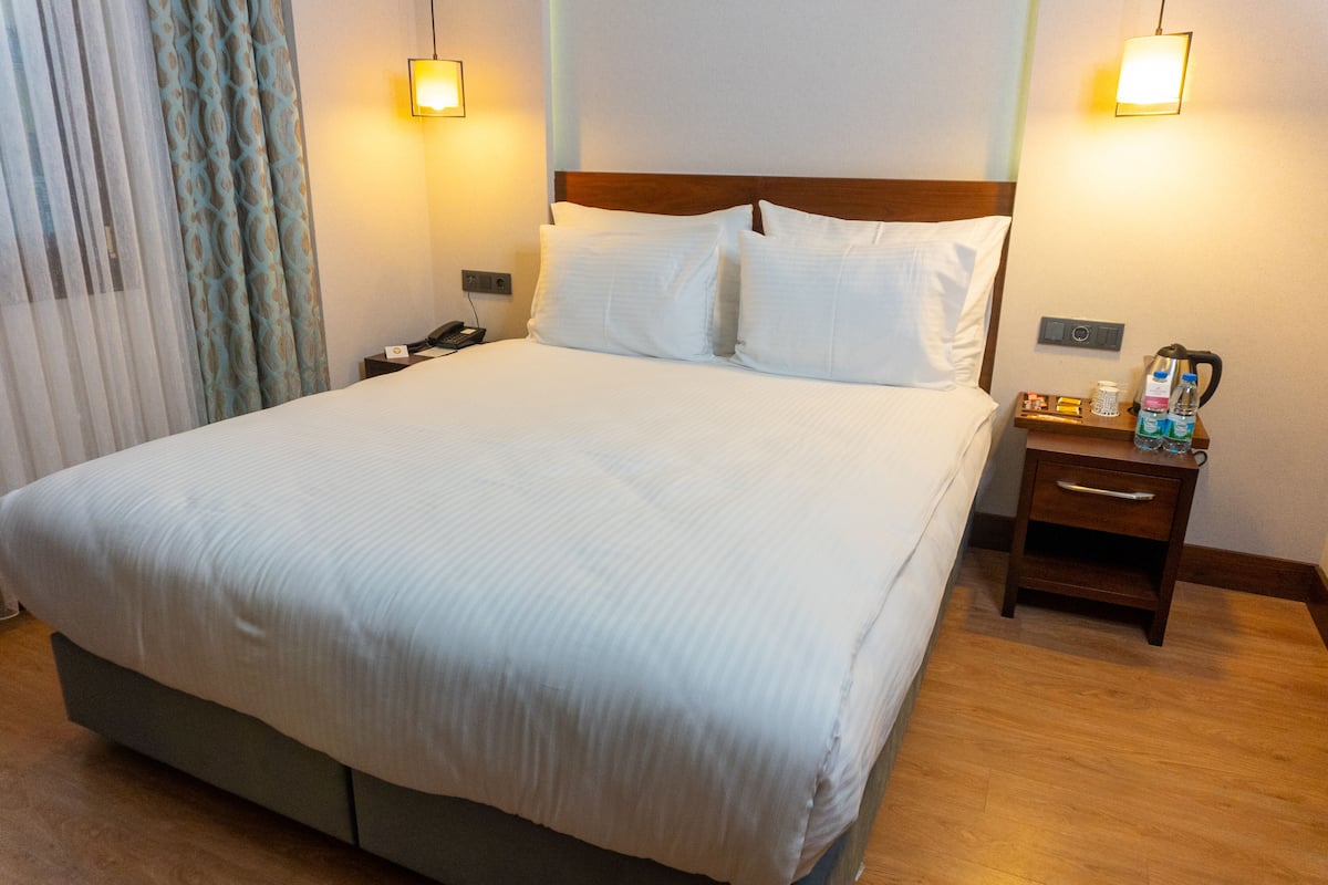 A hotel room with a large bed, two bedside tables, a nightstand, and a wall-mounted lamp.