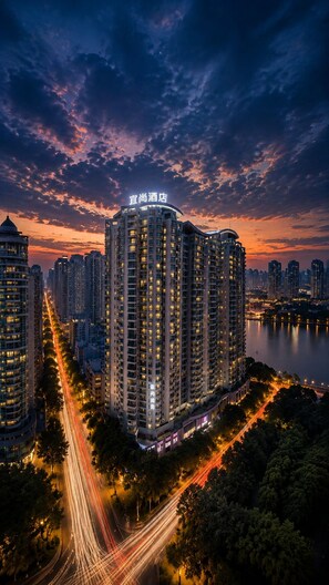 Un hôtel de grande hauteur, reconnaissable à son enseigne imposante, entouré d’un paysage urbain et bordé par un plan d’eau.