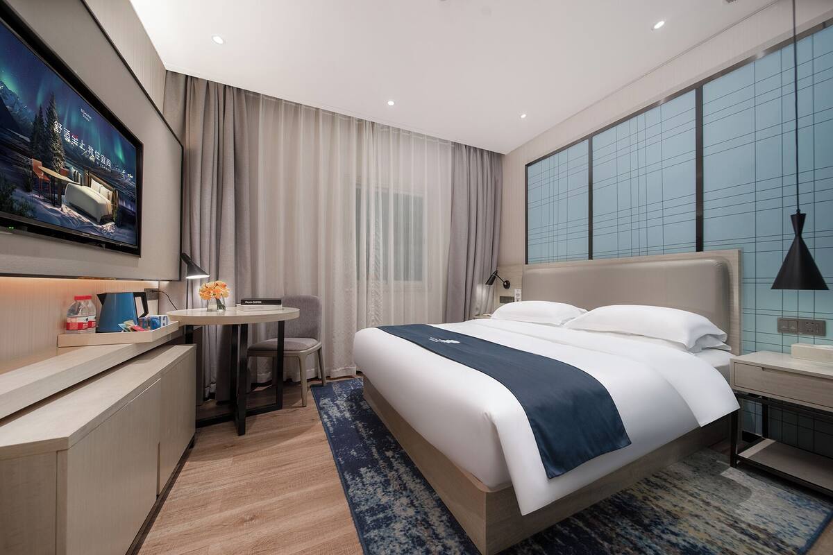 Une chambre d’hôtel moderne avec un grand lit, un bureau et un téléviseur fixé au mur.