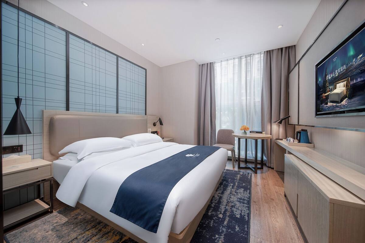 Une chambre d’hôtel moderne, dotée d’un grand lit, d’un bureau, d’une chaise et d’un téléviseur fixé au mur.